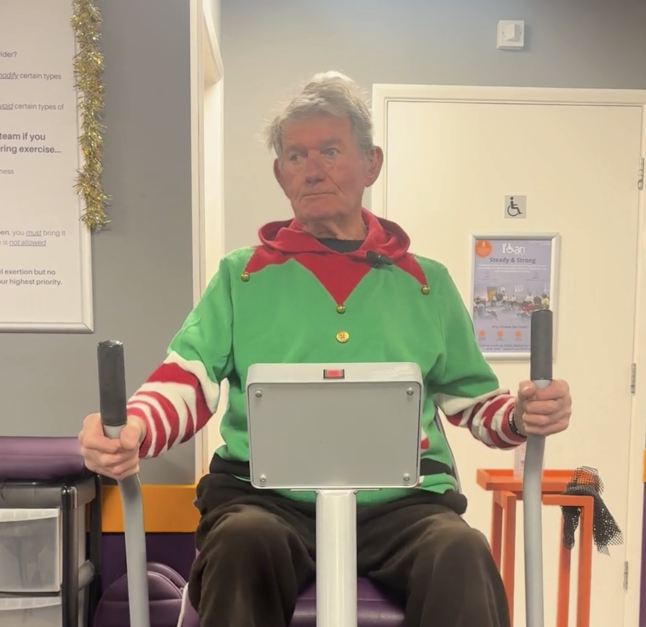 low-impact exercise for seniors at I Can Move More, elderly man using elliptical machine, staying active, improving mobility and strength, adult fitness, holiday-themed workout attire, senior wellness program