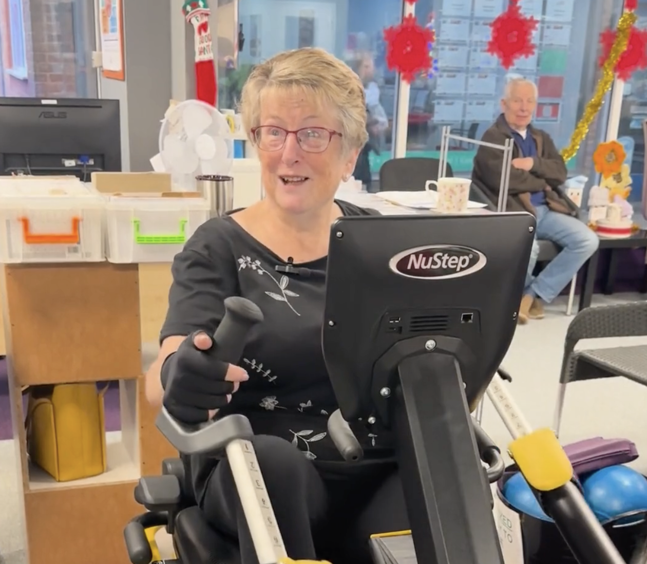 Elevated view of a smiling woman enjoying a fitness session on a NuStep recumbent cross trainer at a community wellness center, promoting physical activity and movement for seniors and individuals with mobility challenges.