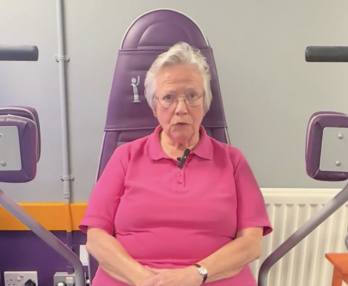 elderly woman exercising on adaptive fitness equipment in a rehabilitation or physiotherapy setting for improving mobility and strength in seniors